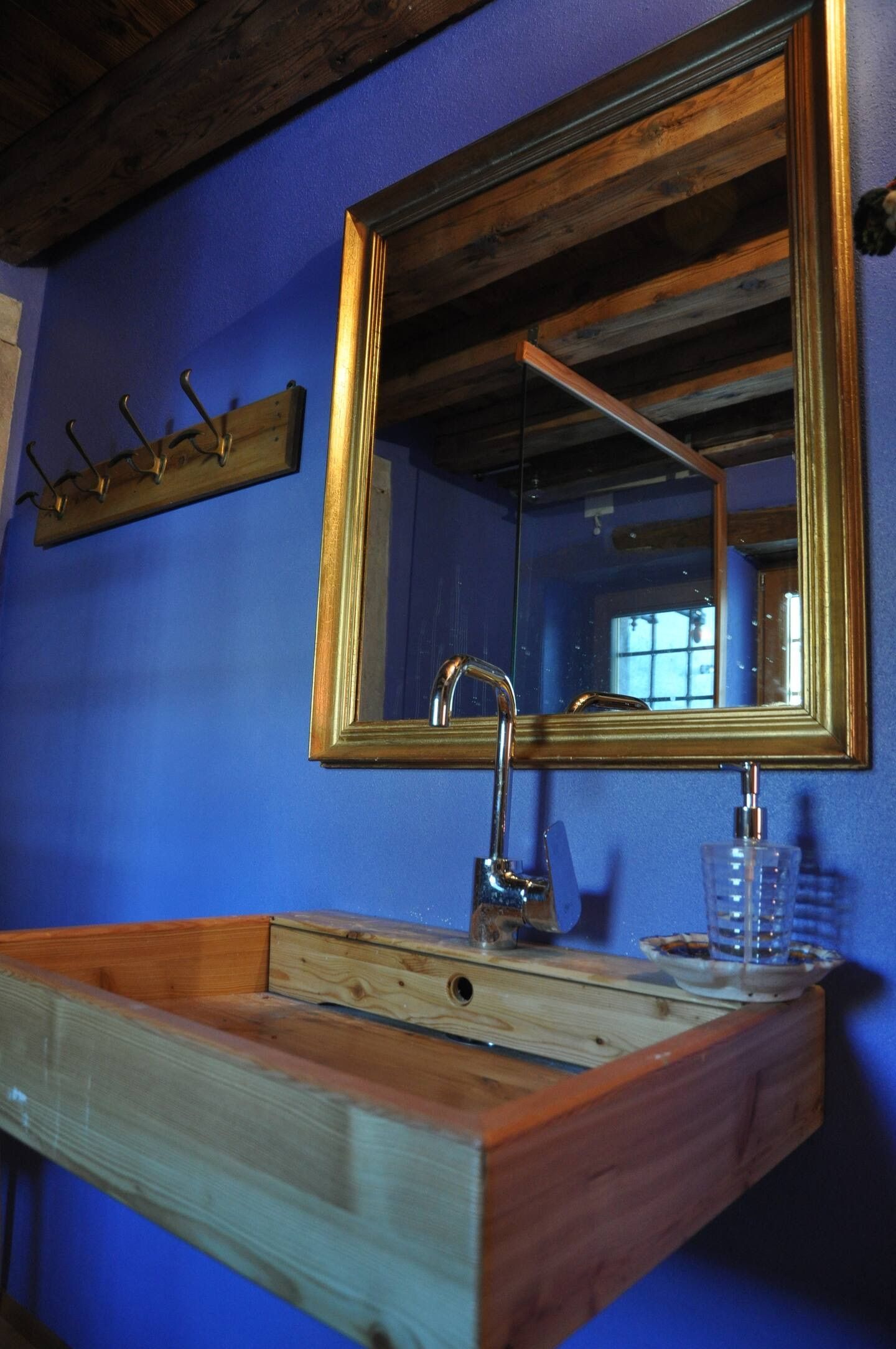 Mobiletto in legno con rubinetto argentato, specchio con cornice dorata e parete blu.