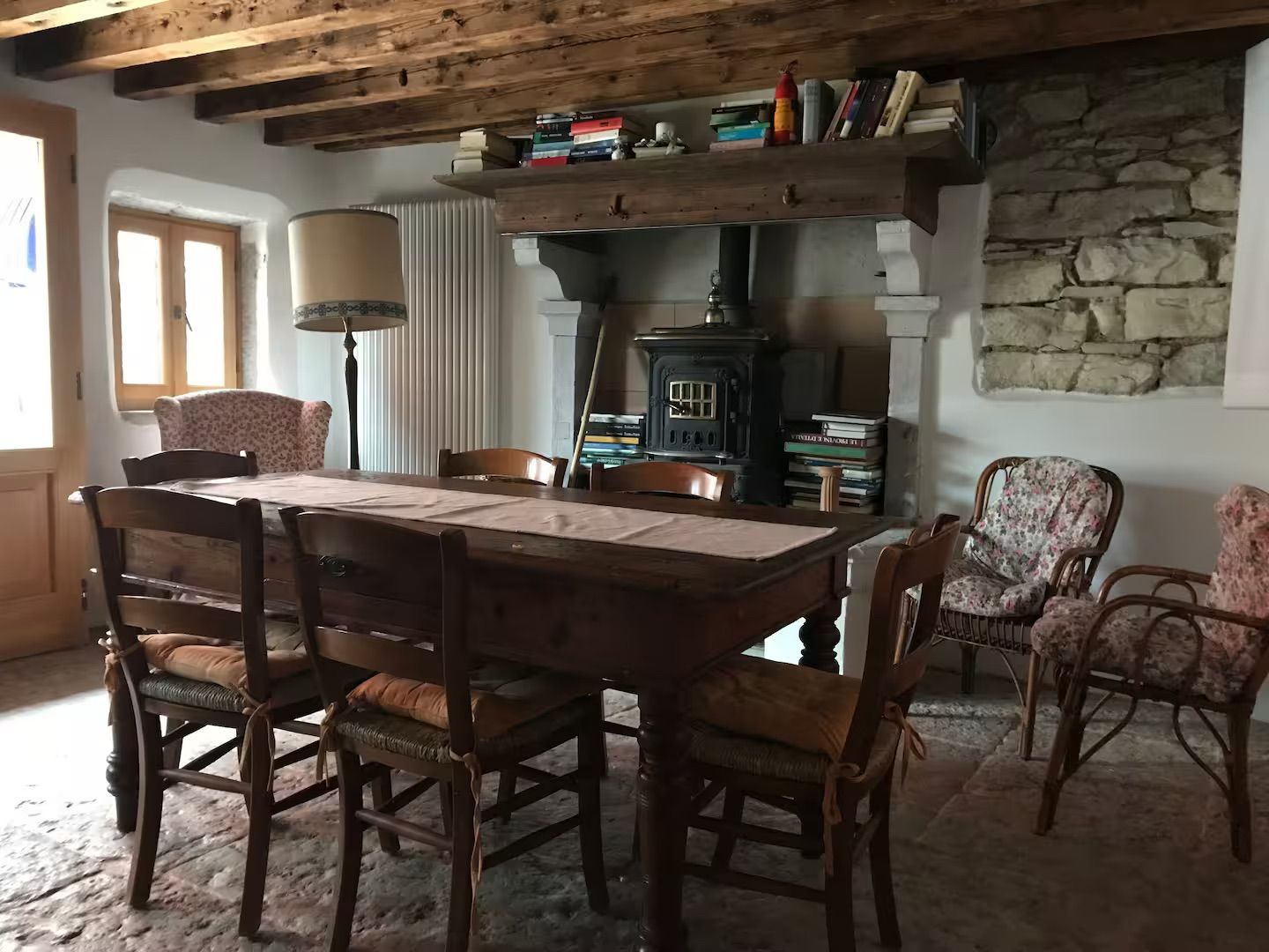 Sala da pranzo con tavolo in legno, sedie, camino, parete in pietra e librerie.