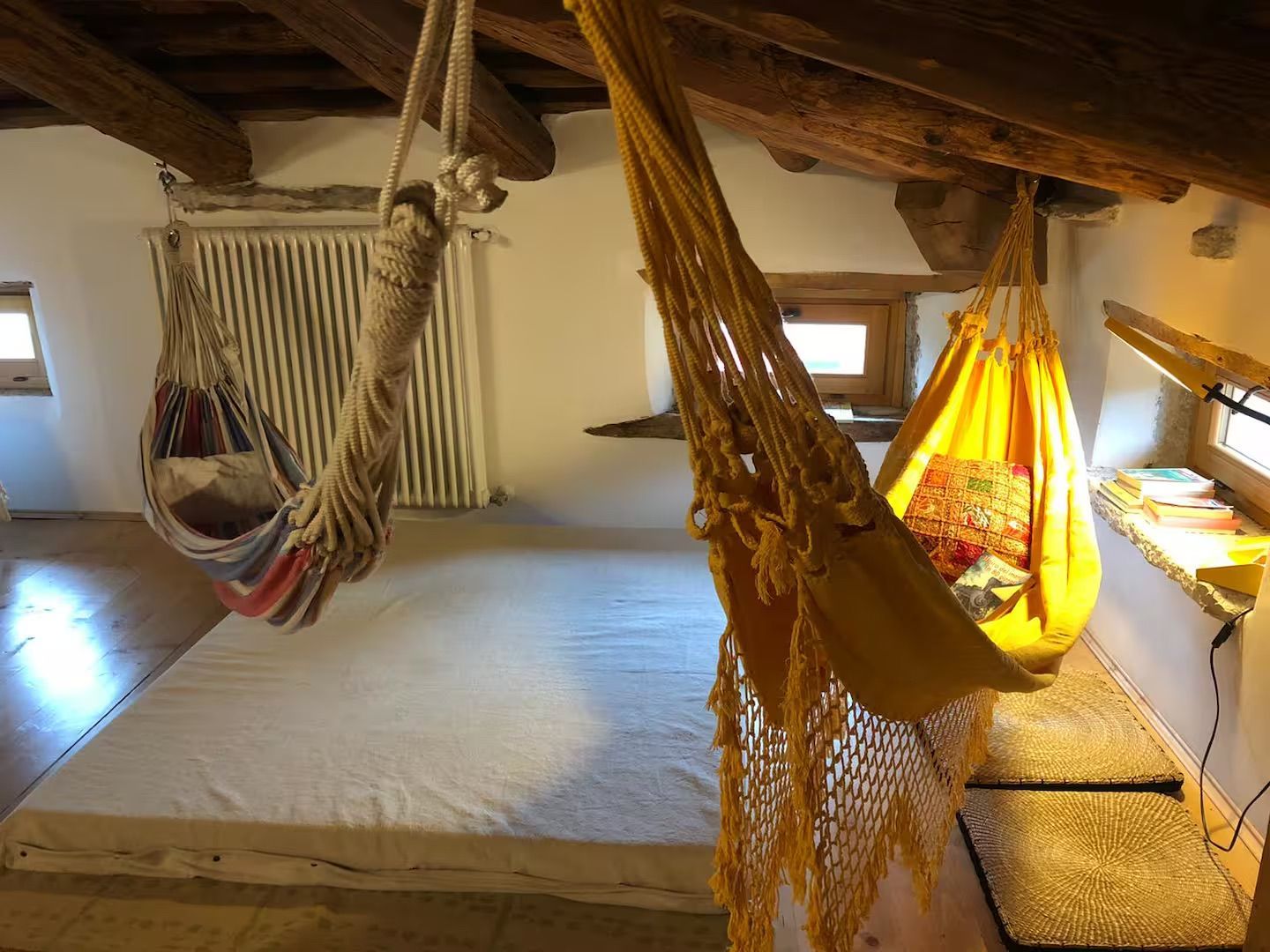 Accogliente mansarda con due amache sospese su un grande materasso. Travi in legno.
