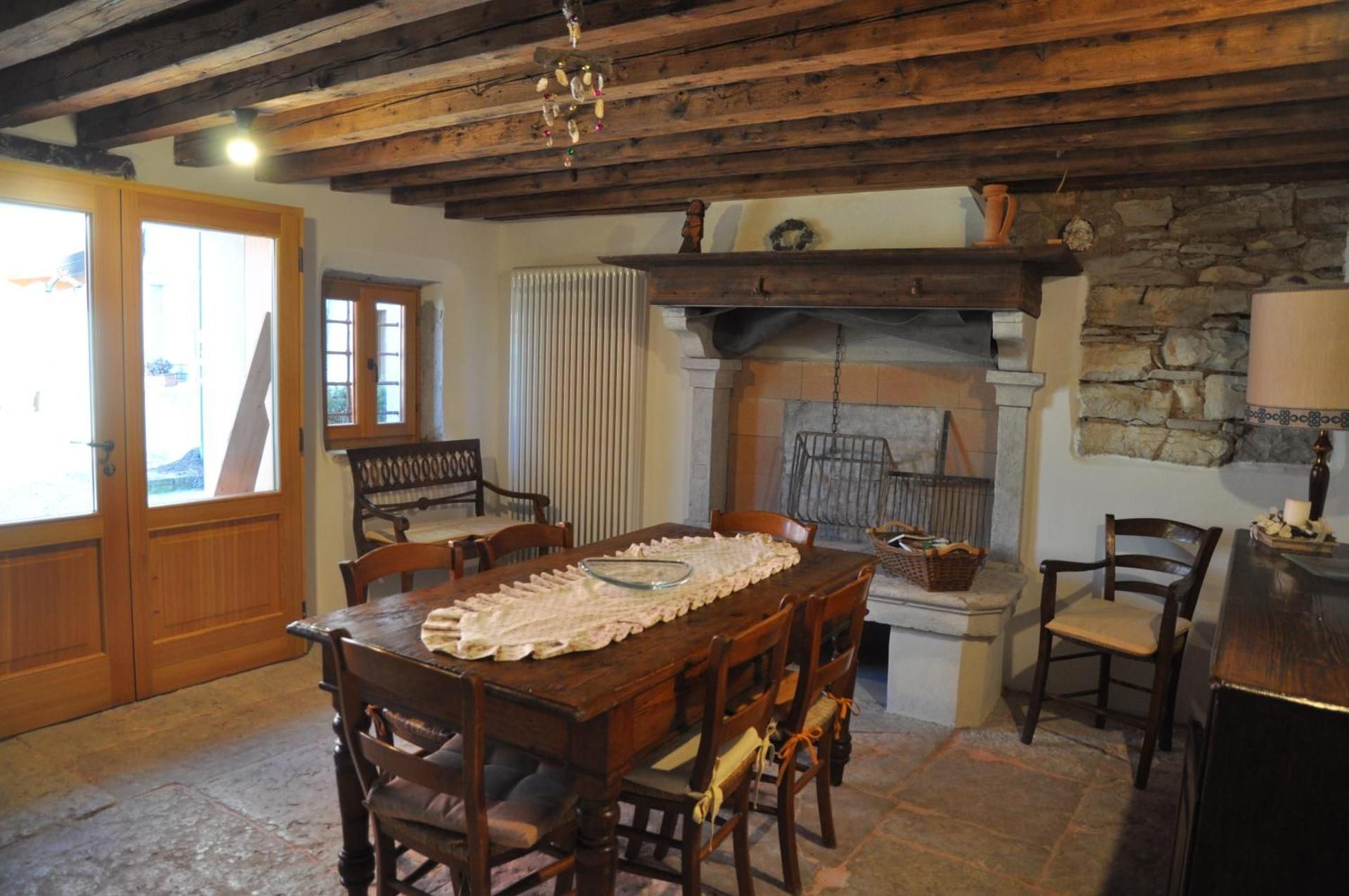 Sala da pranzo con tavolo in legno, sedie, camino e travi a vista.