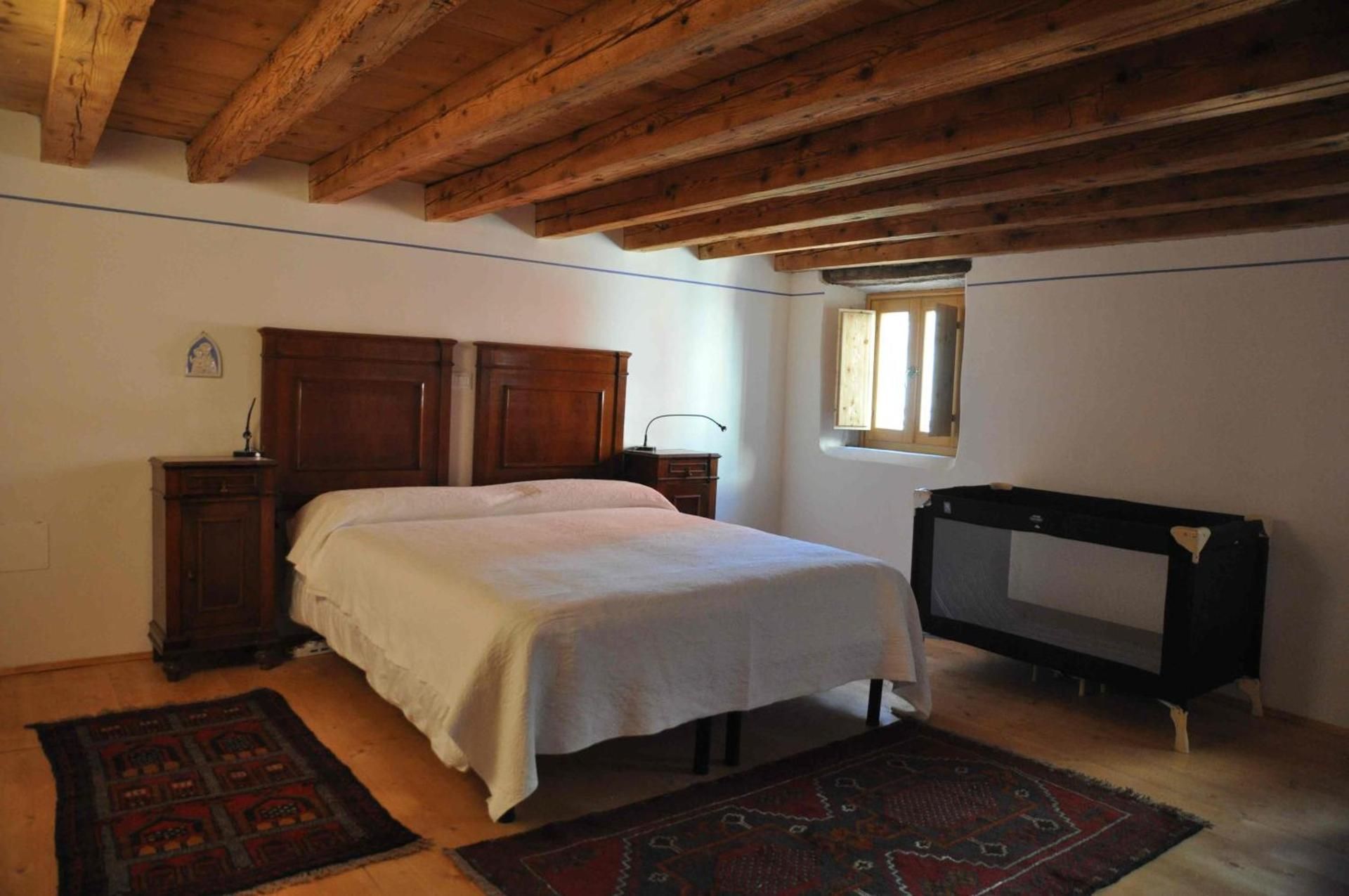 Camera da letto con soffitto con travi in legno, letto, comodini, tappeti e box per bambini.