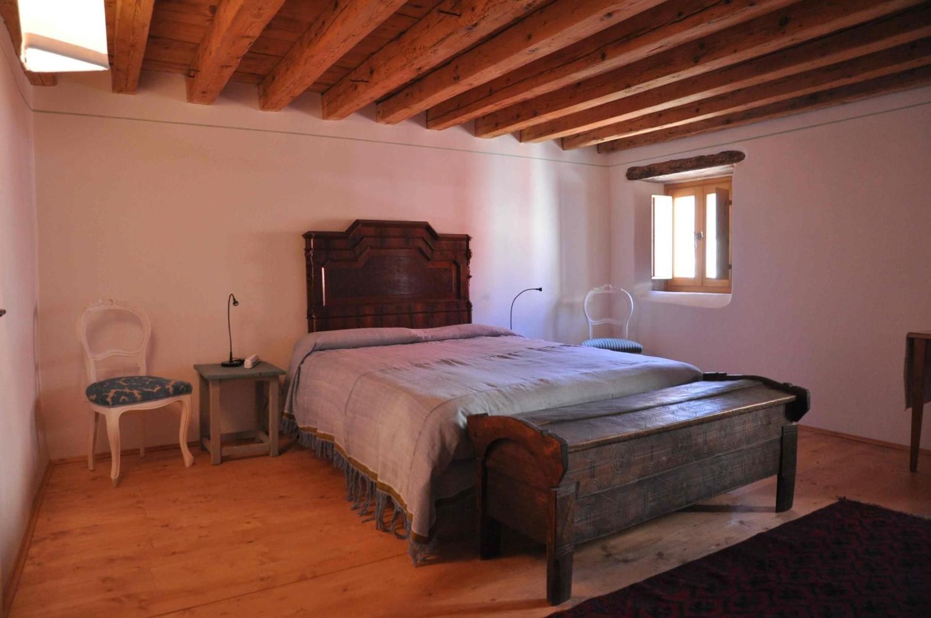 Camera da letto con letto in legno, baule, pareti bianche e soffitto con travi in legno.