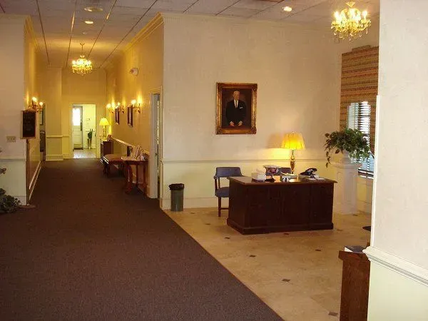 Dimly lit lobby hallway with carpet, tiled floor, desk, chairs, and a lamp-lit reception area