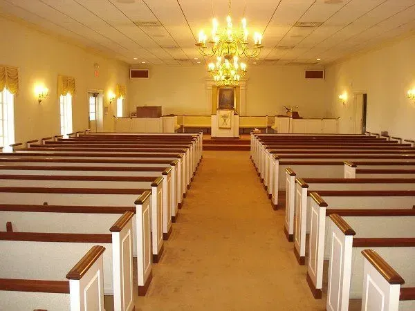 Empty church sanctuary with wooden pews facing a pulpit and chandeliers