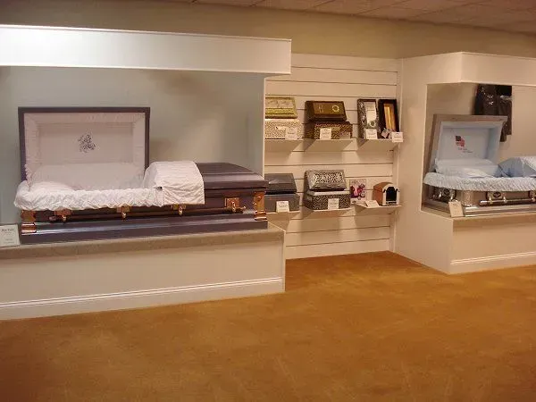Casket showroom with bed displays and shelves on a tan carpeted floor.