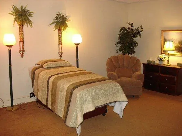 Cozy room with a single bed, armchair, lamps, wall decor, and a dresser with a mirror.