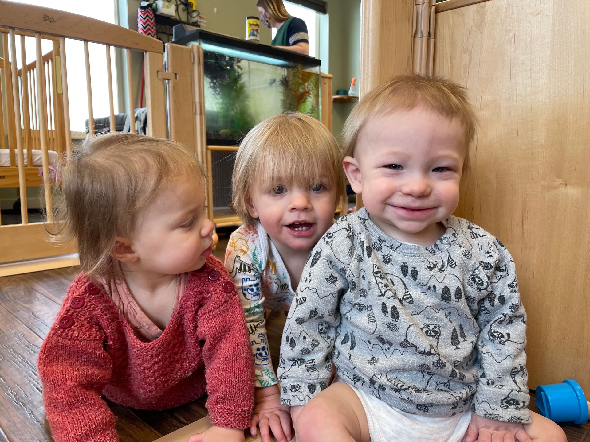 Three young children sitting on a couch, smiling in a bright indoor room.