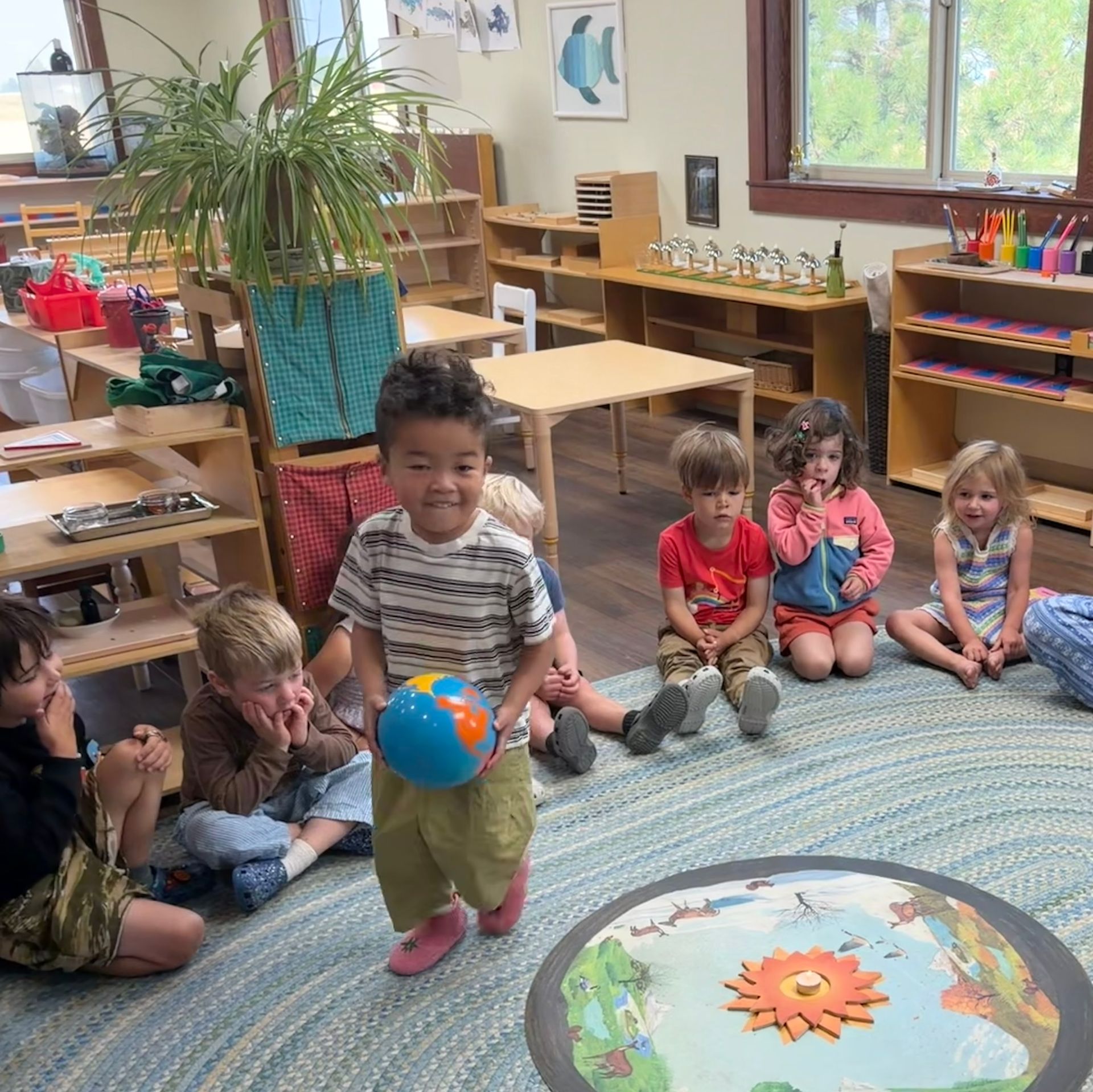 Children sitting and playing in a colorful classroom, one holding a globe.
