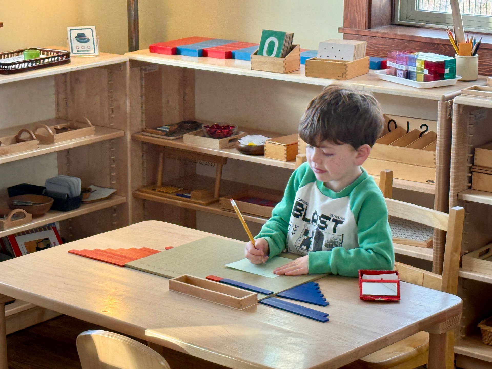 Child writing on sheet of paper on top of a wooden desk.