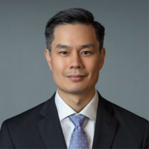 Man in a blue dress shirt and patterned tie smiling.