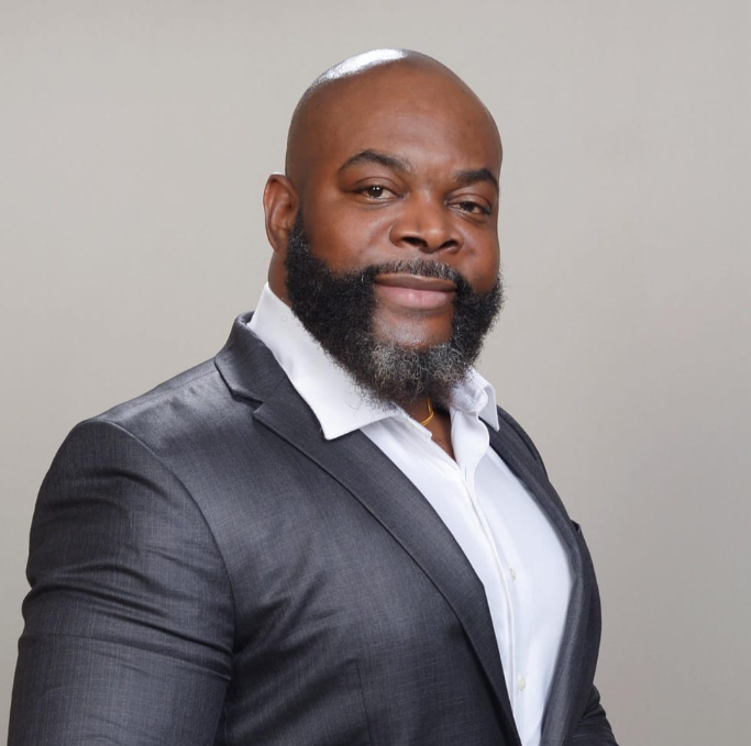 Bald man with a full beard, wearing a suit and white shirt, smiling.