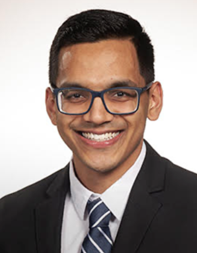 Bald man wearing glasses, a suit, and tie looking forward.