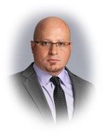 Bald man wearing glasses, a suit, and tie looking forward.