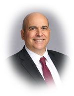 Man in suit and tie smiling, standing against a blurred background.