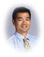 Man in a blue dress shirt and patterned tie smiling.