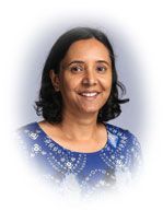 Woman with short dark hair, smiling, wearing a blue patterned top, against a blurred background.