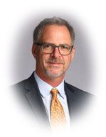 Man in glasses, suit, and tie; smiling, portrait style.