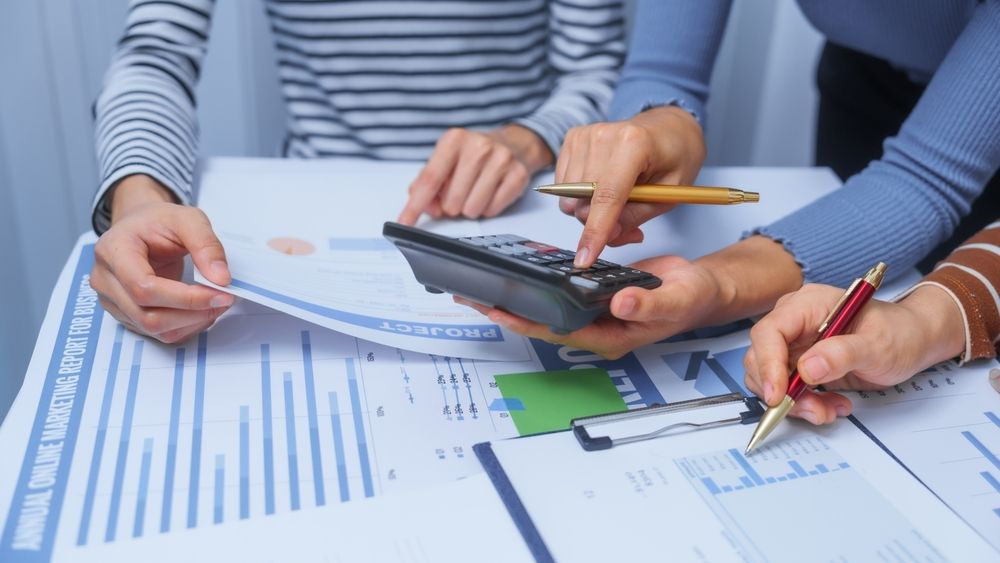 Hands using calculator and pencil over financial charts and documents on a desk