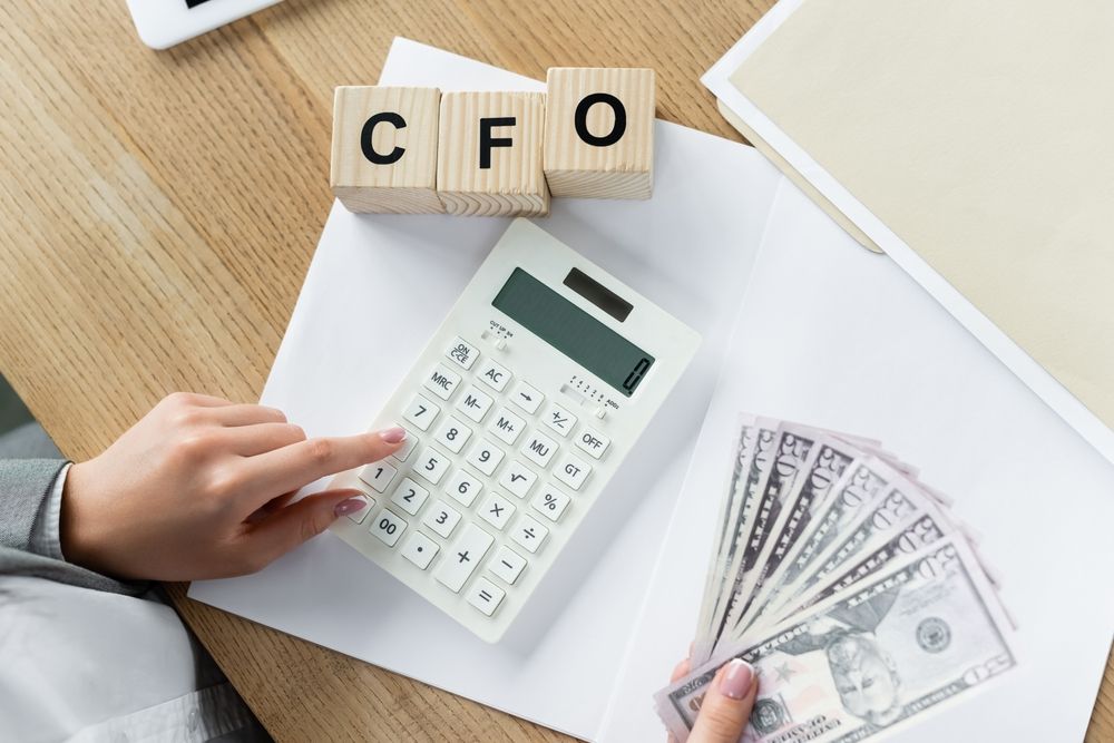 Hands using a calculator with cash beside CFO letter blocks on a desk