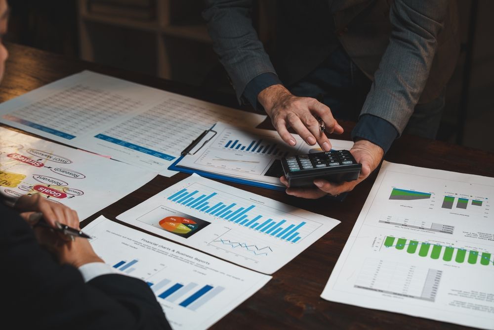 Hands reviewing charts and a calculator at a desk with printed business reports and graphs