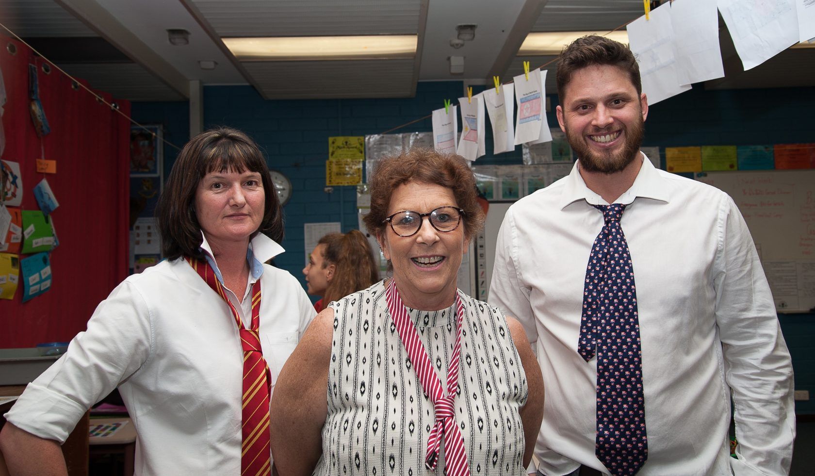 Three people wearing ties are posing for a picture in a classroom.