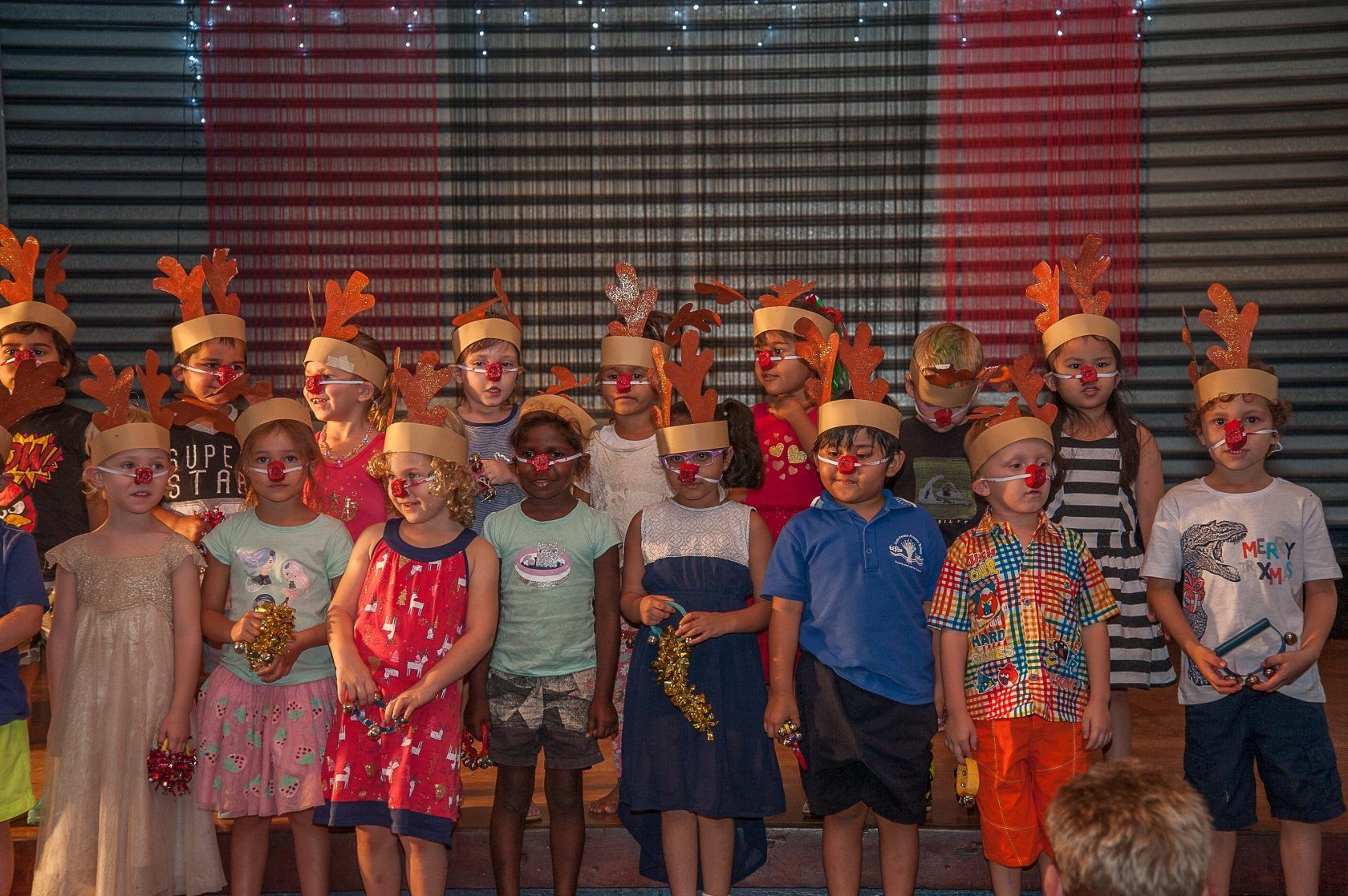 A group of children wearing reindeer hats and red noses are standing on a stage.