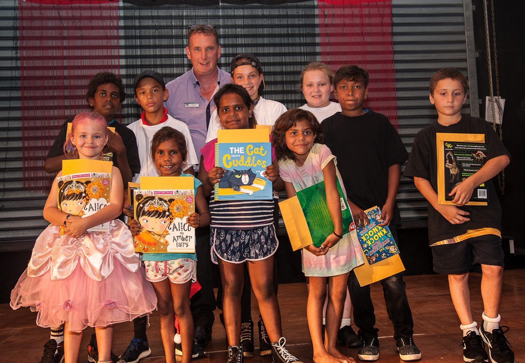 A group of children are posing for a picture and one of them is holding a book that says ' a cat ' on it