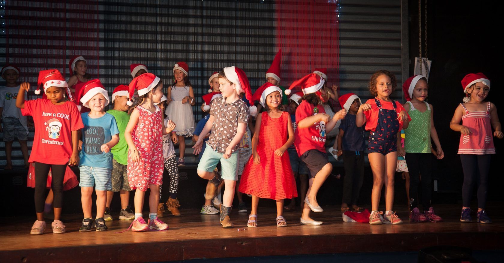 A group of children are standing on a stage wearing santa hats.