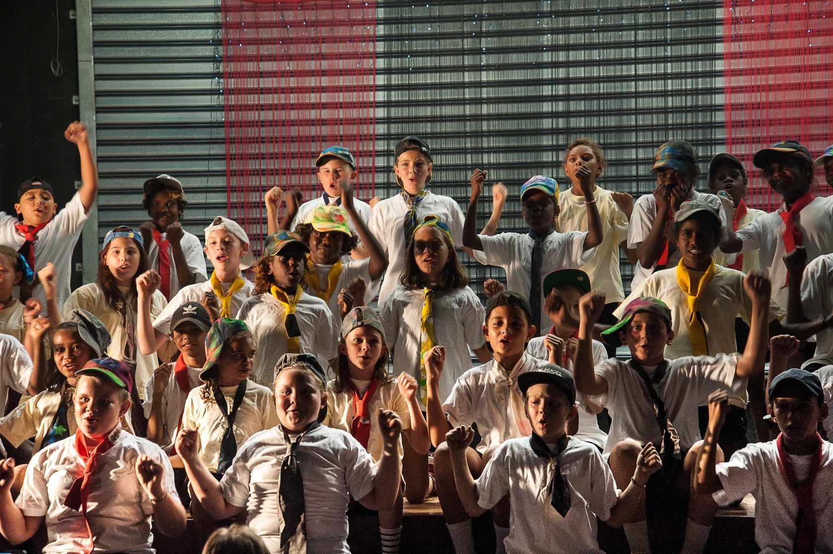 A large group of children are standing in front of a wall with their hands in the air.