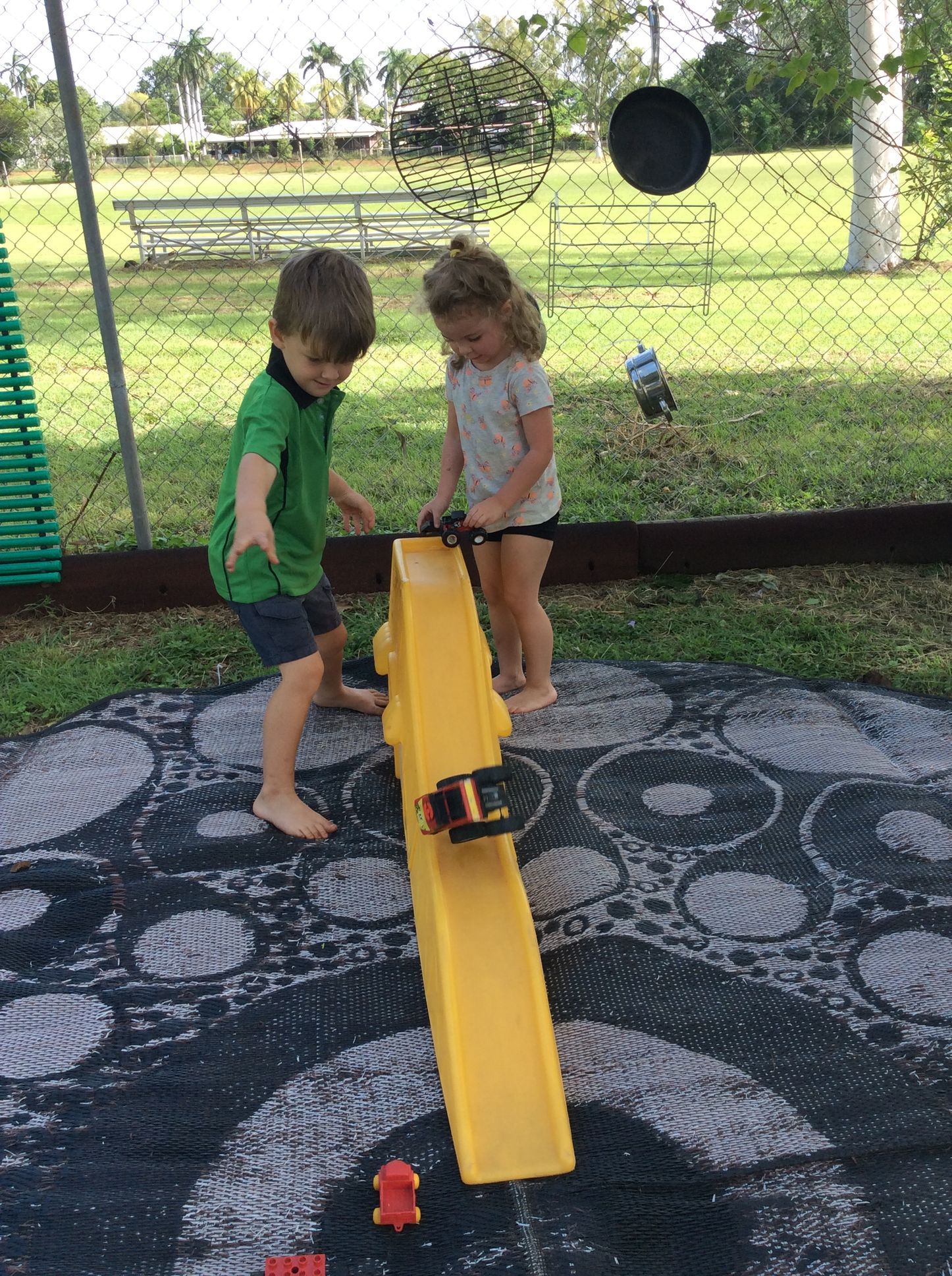A boy and a girl are playing on a yellow seesaw.