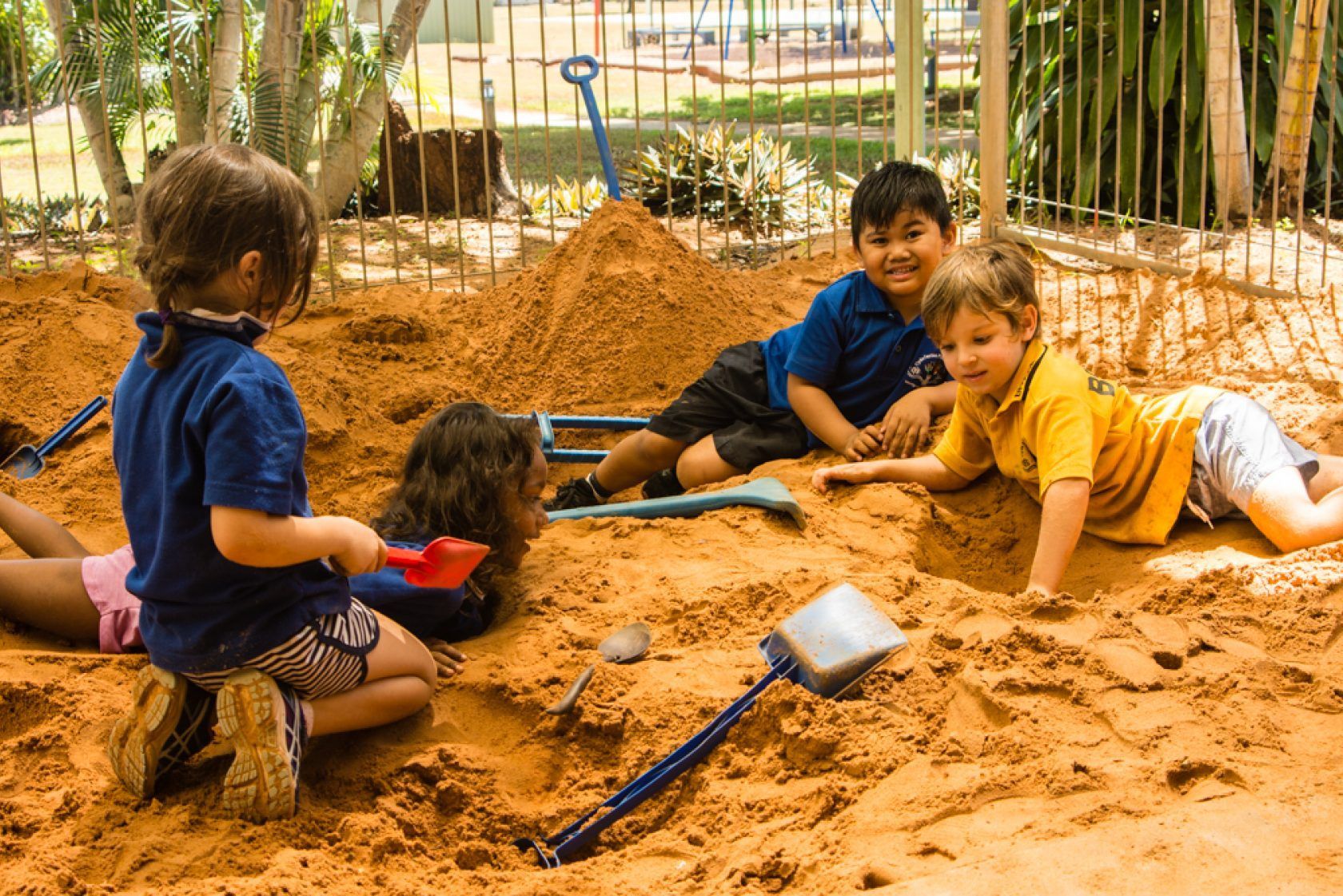 A group of children are playing in a sandbox with shovels.