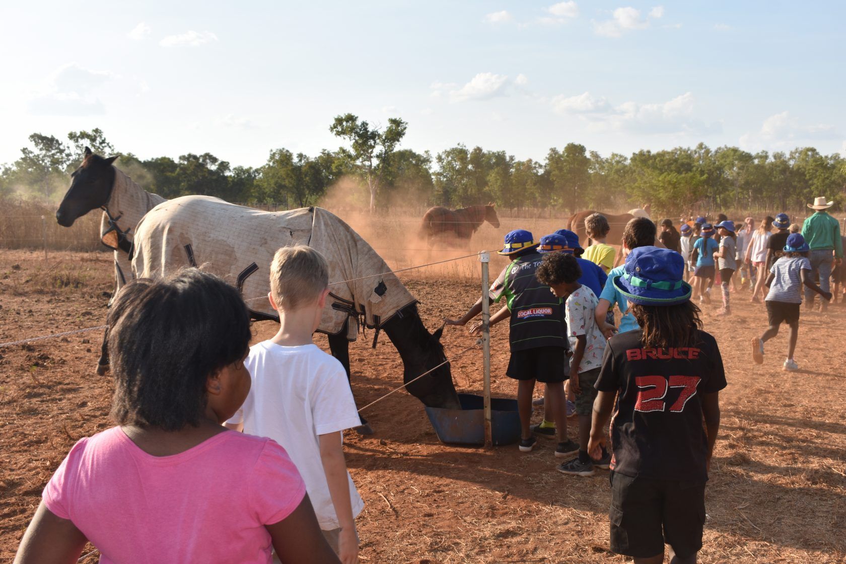 A group of children are standing around a horse in a dirt field.