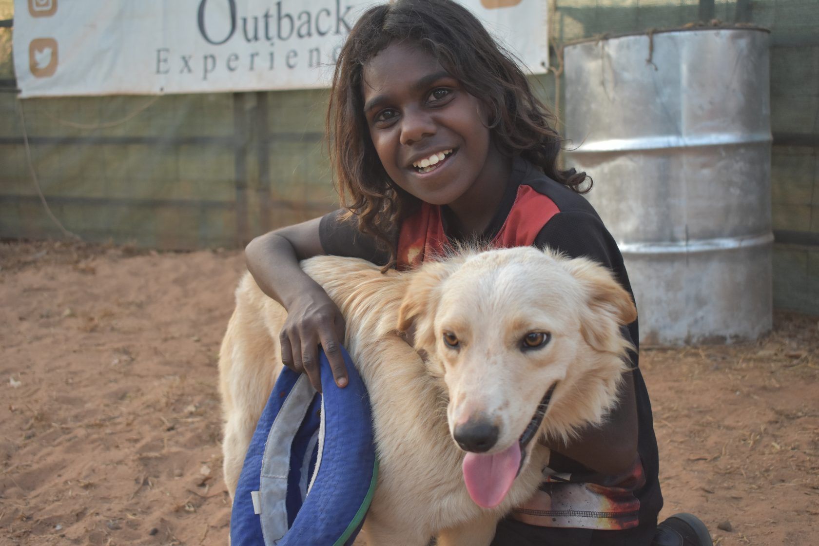A young girl is holding a dog in front of a sign that says outback experience