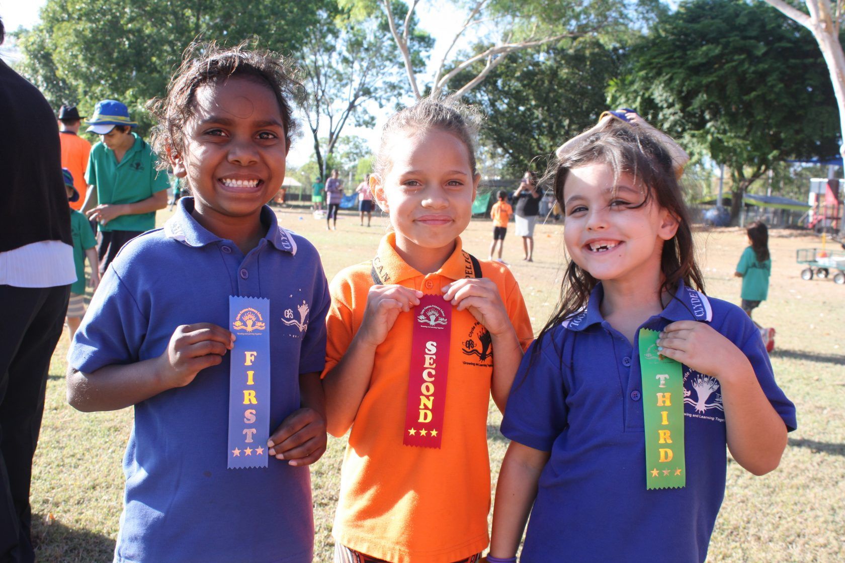 Three young girls holding ribbons that say first second and third