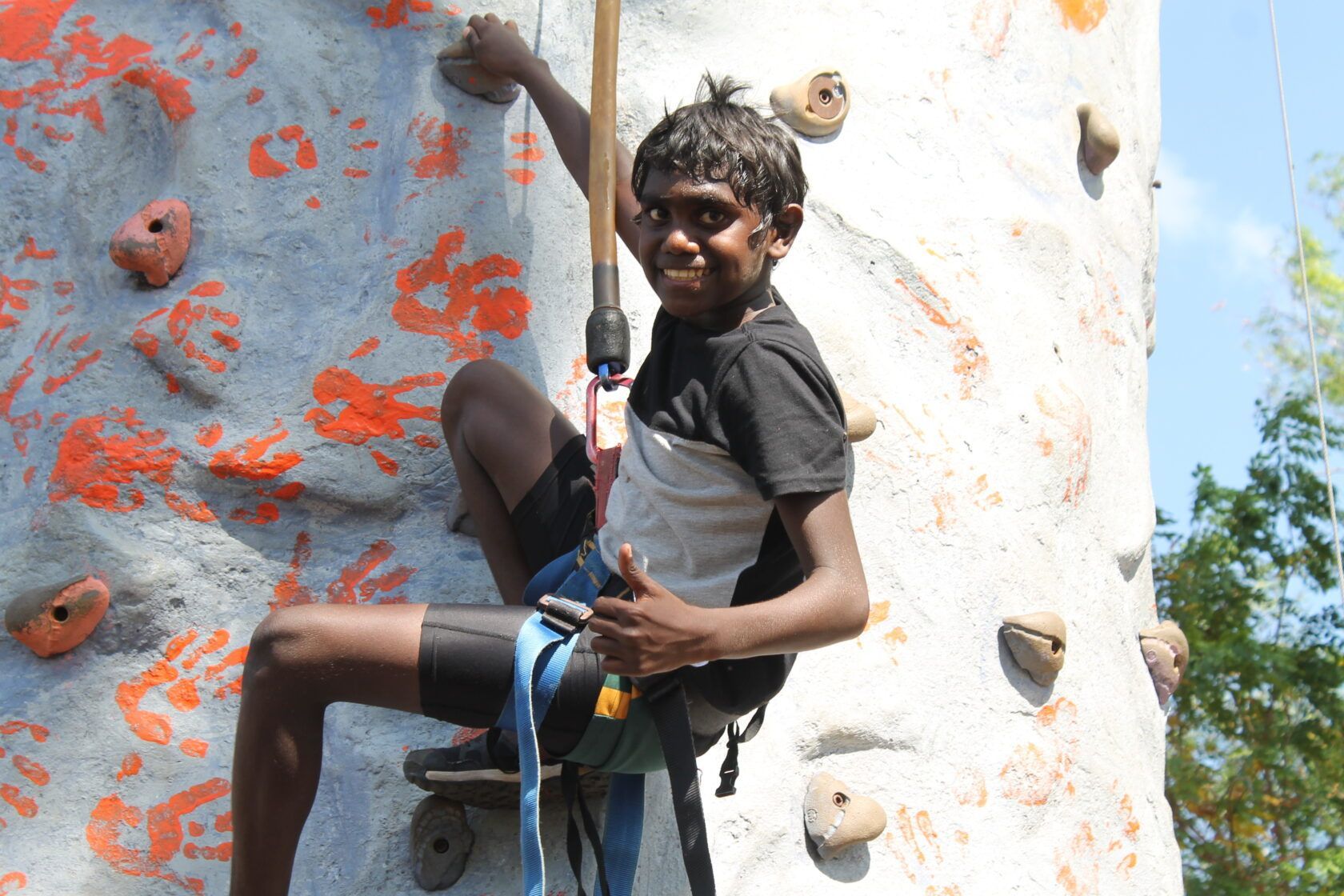 A man is climbing a rock wall and giving a thumbs up