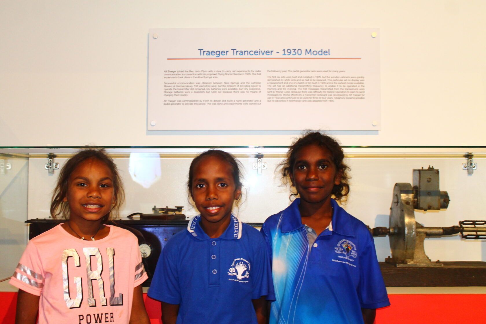 Three young girls are posing for a picture in front of a display case.