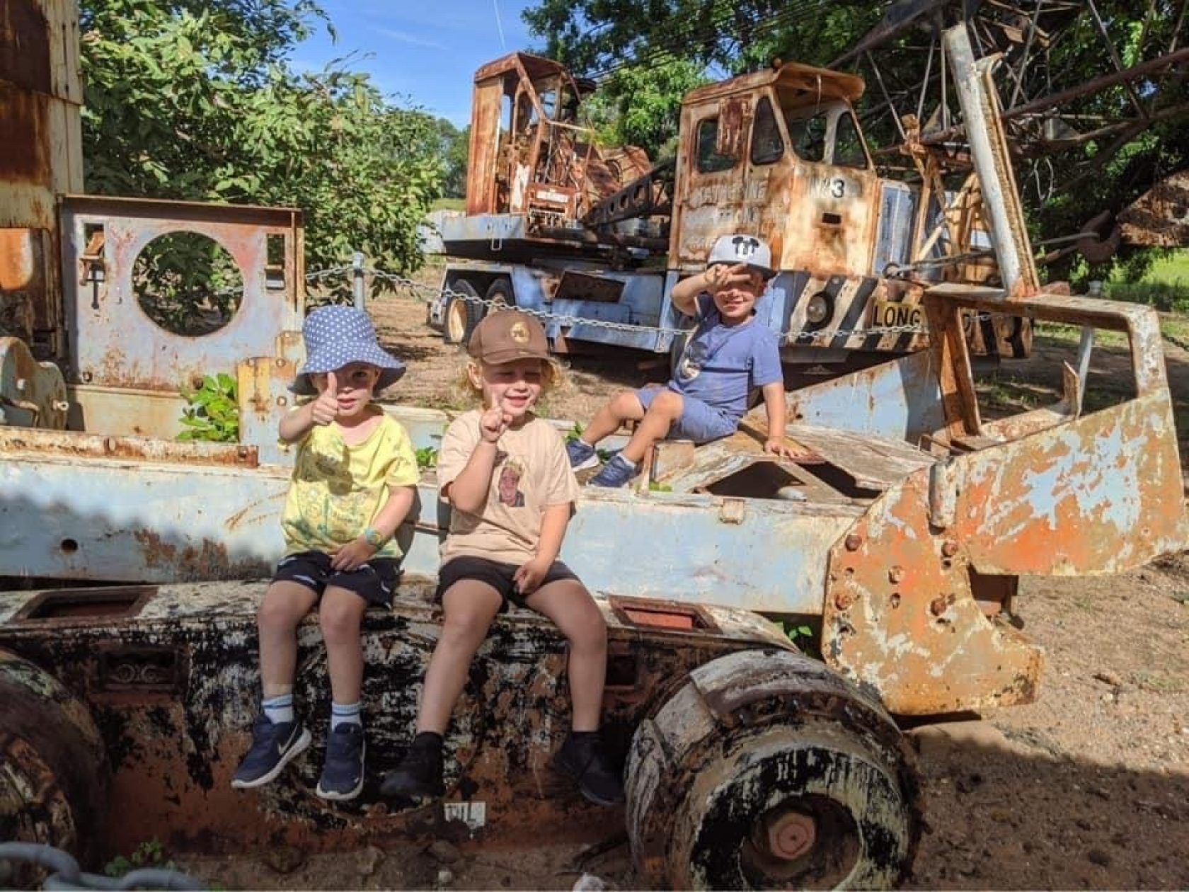 Three young boys are sitting on top of a rusty truck.