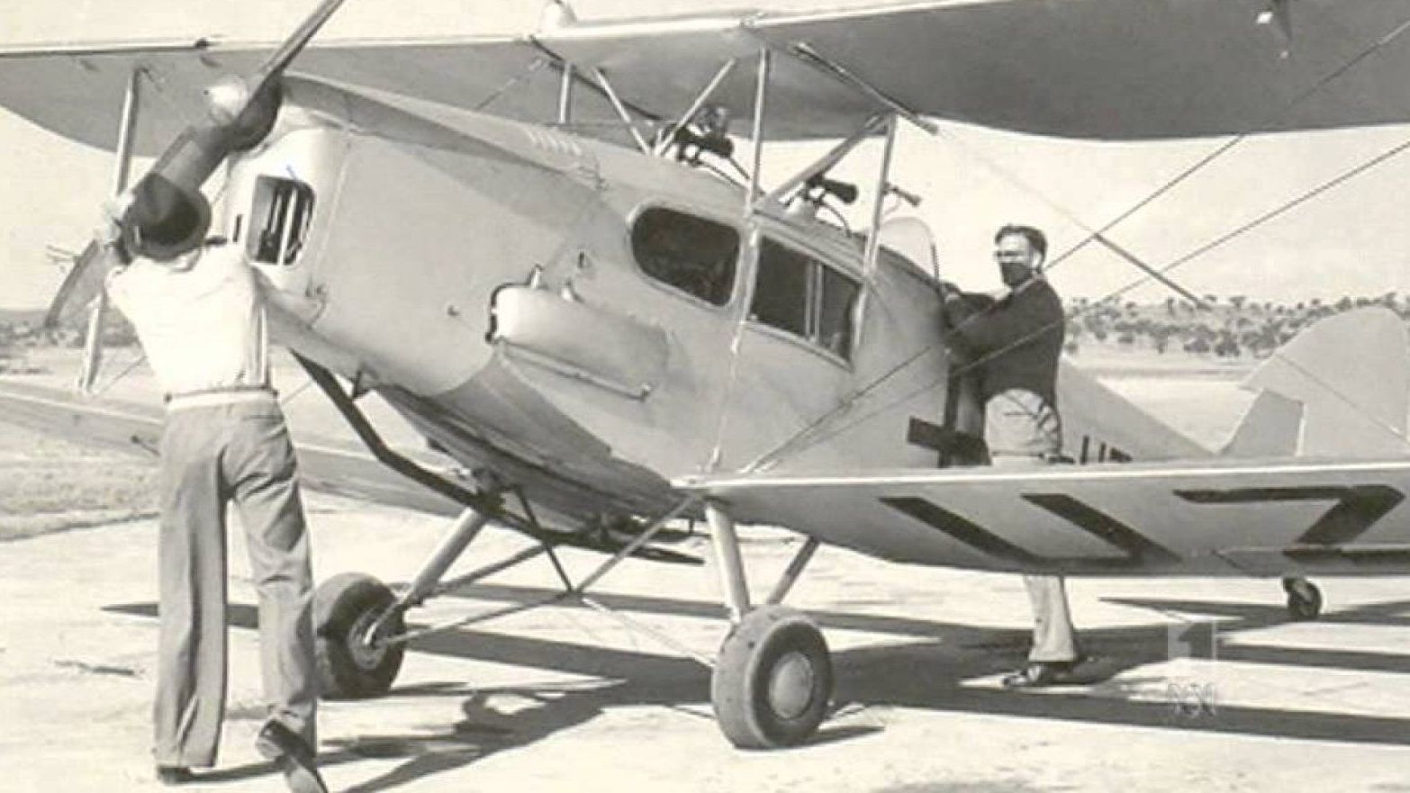 A black and white photo of two men working on an airplane