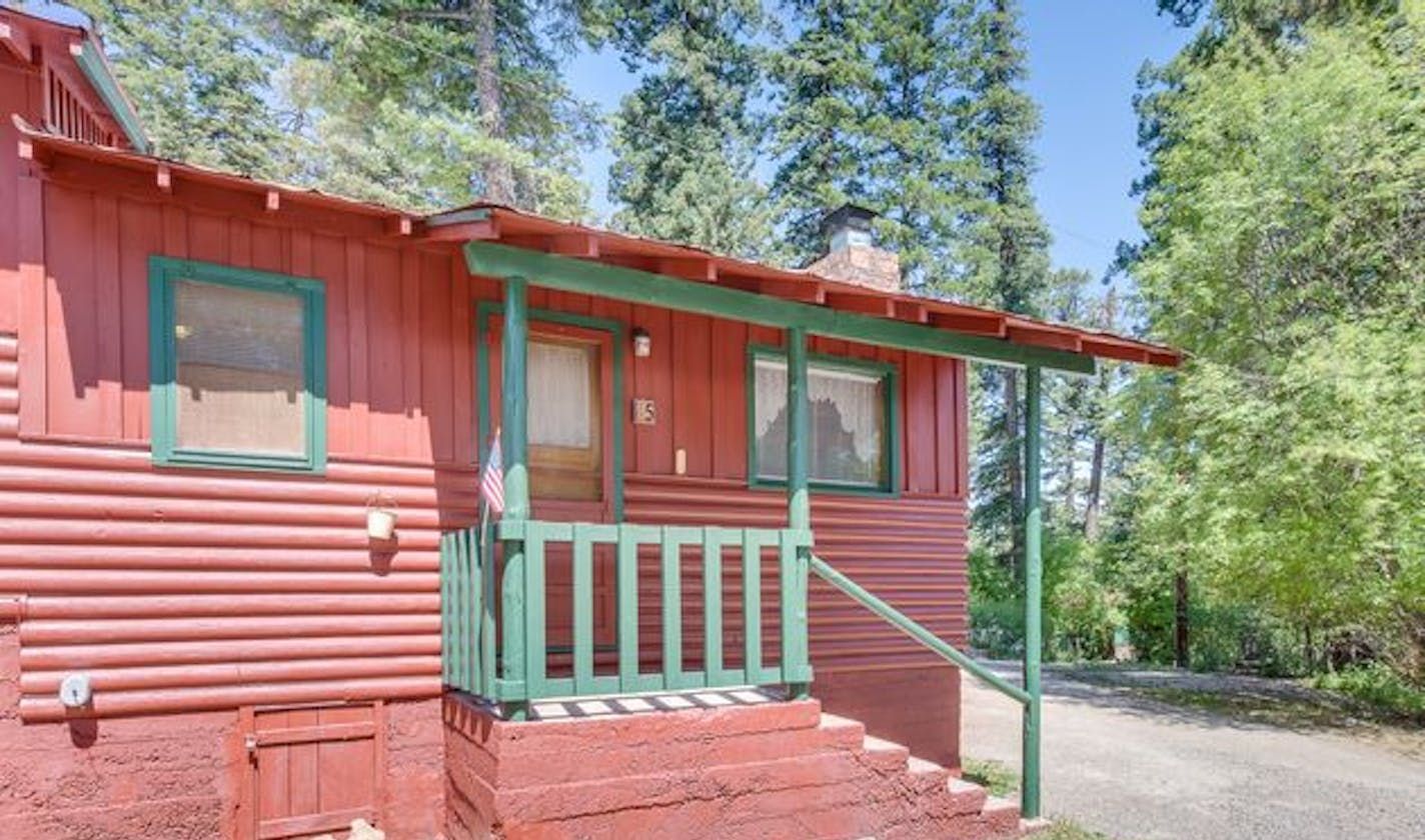 A red cabin with green trim and a front porch steps leading up to a door, situated in a forested area.