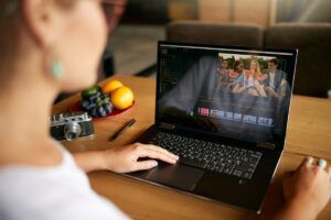 Person using a laptop at a table, watching a video on screen beside a bowl of fruit.