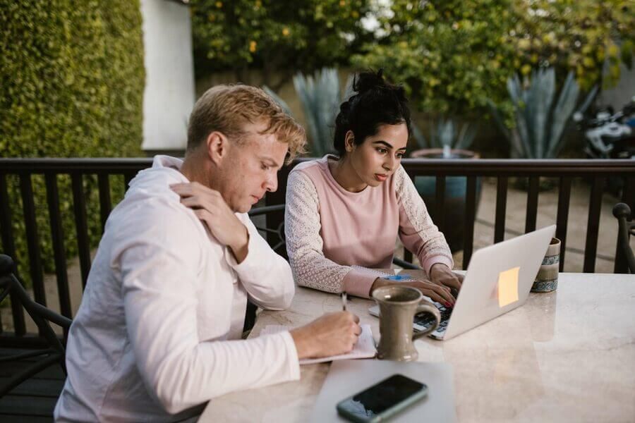 Two people working on a laptop at an outdoor table, with a coffee mug and phone nearby.