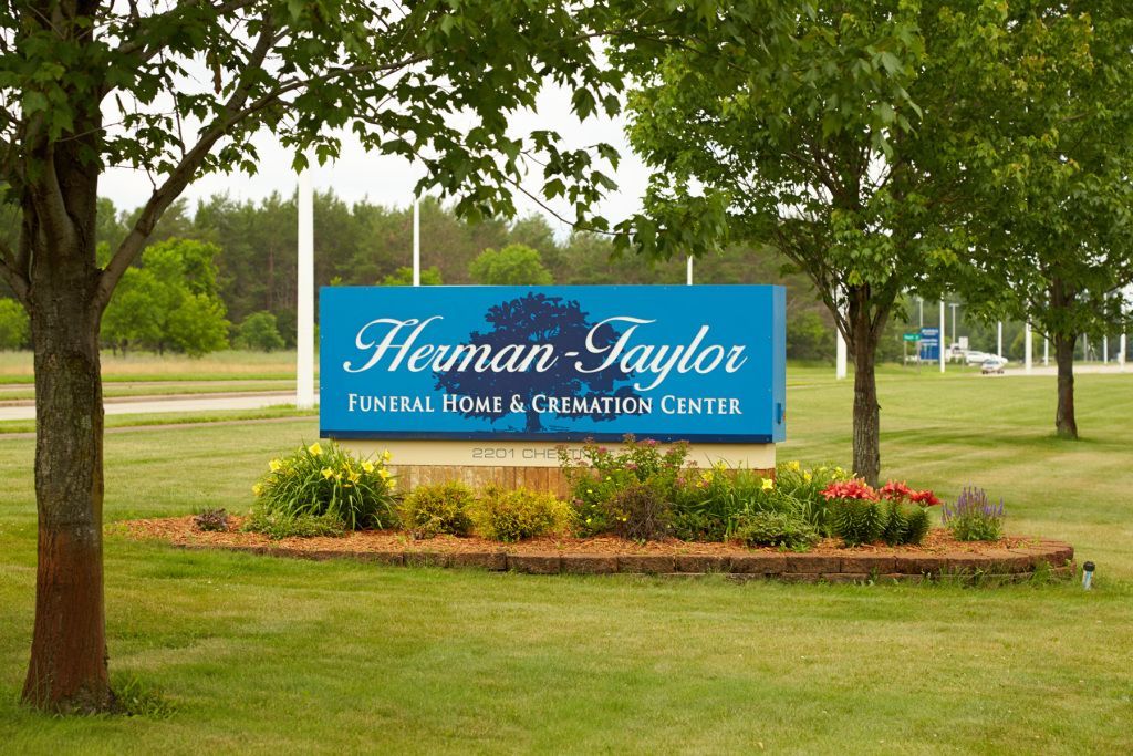 Blue sign for Herman Taylor Funeral Home & Cremation Center in a landscaped park-like setting