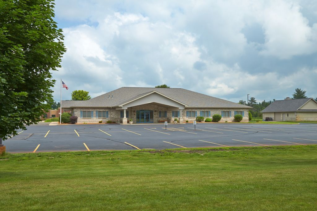 Single-story building with a gray roof and empty parking lot under a cloudy sky