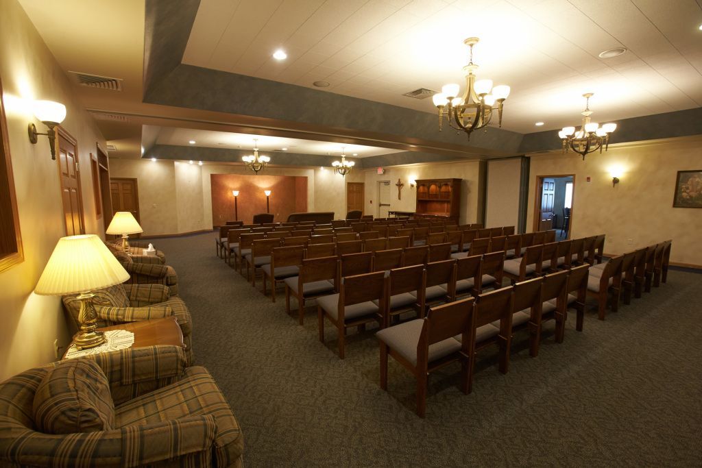 Empty banquet hall with rows of wooden chairs, warm lighting, and beige carpet