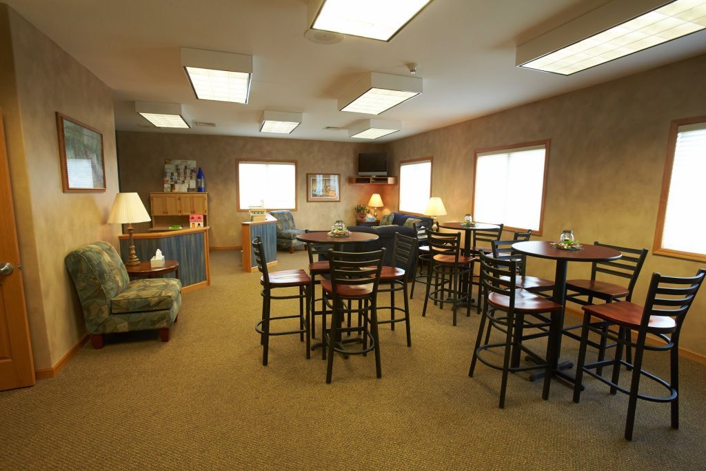 Quiet lounge with tables and chairs, carpeted floor, windows, and a seating area with a couch and lamp