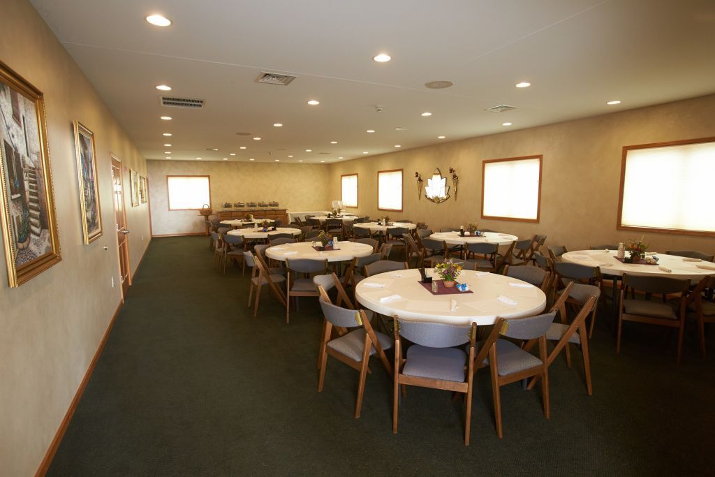 Empty banquet room with round tables, white tablecloths, and tan chairs under warm ceiling lights
