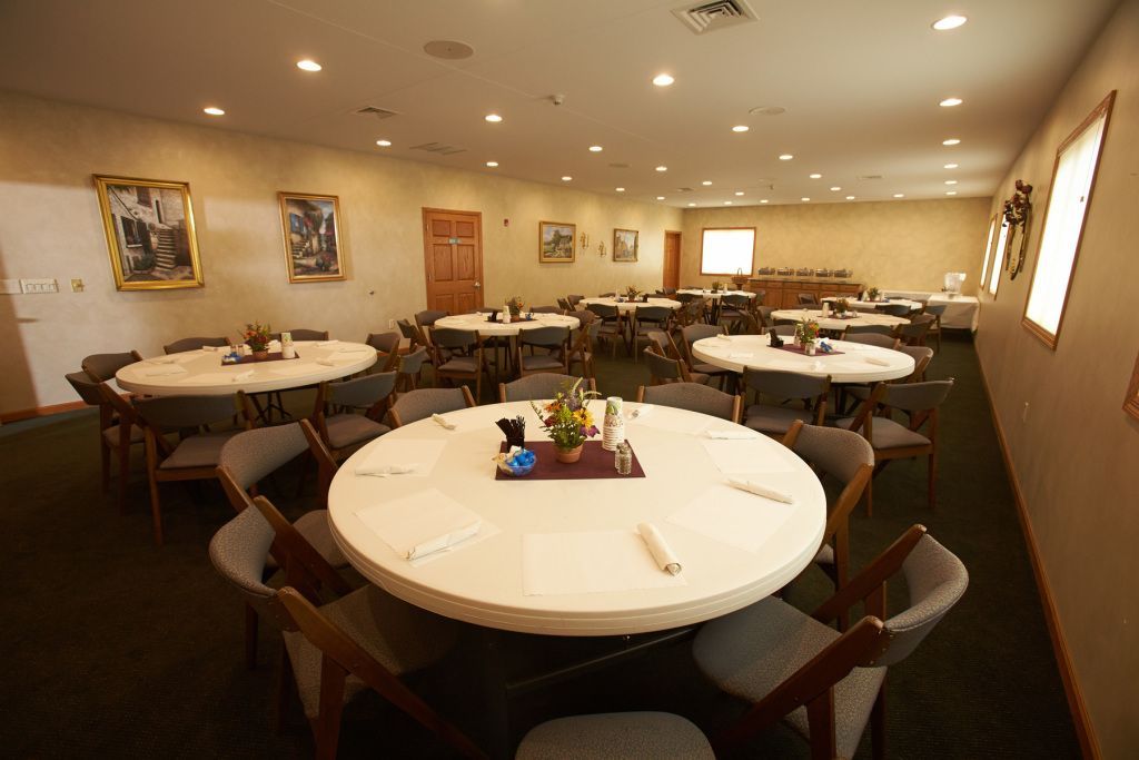 Round banquet hall with white-tablecloth tables, brown chairs, and framed wall art under warm ceiling lights.