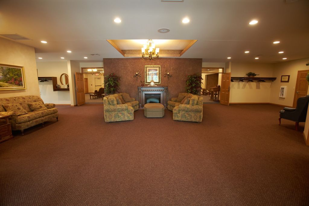 Spacious hotel lobby with carpet, sofas, and chairs around a fireplace beneath warm ceiling lights