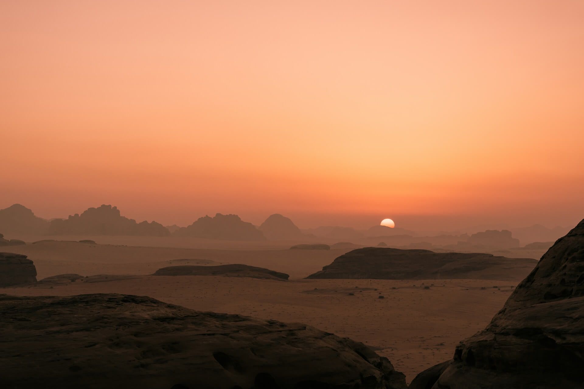 Sunset over a rocky desert landscape with hazy distant hills and an orange sky