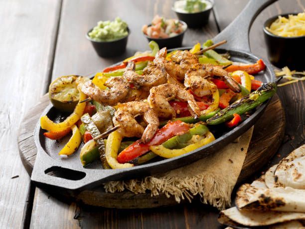Shrimp fajitas on sizzling cast iron skillet with bell peppers, tortillas, and toppings.
